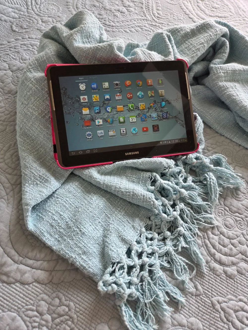 A tablet resting on a soft teal throw on a bed at home