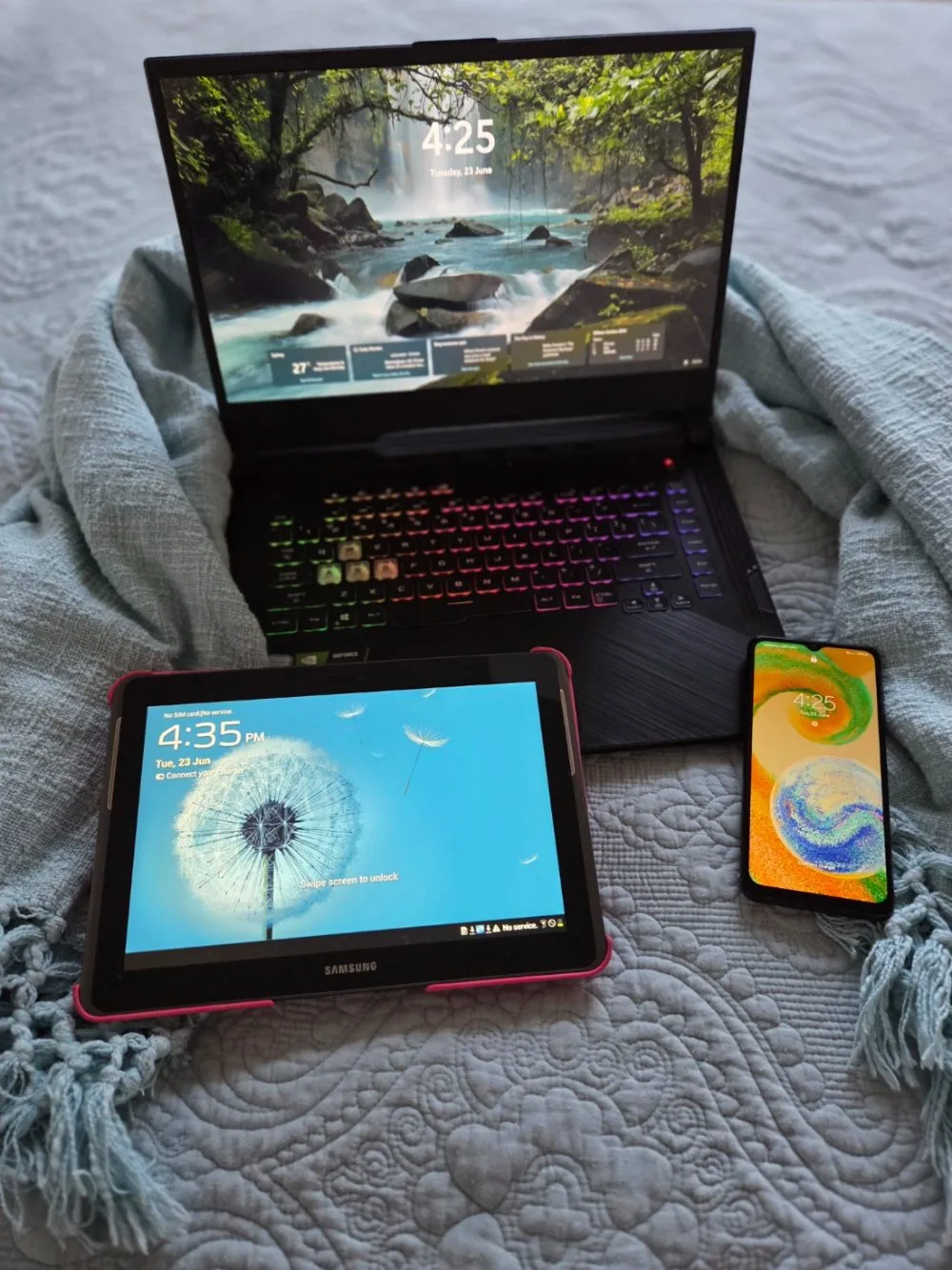 A laptop, tablet and phone with calm screens on a bed with a soft teal throw