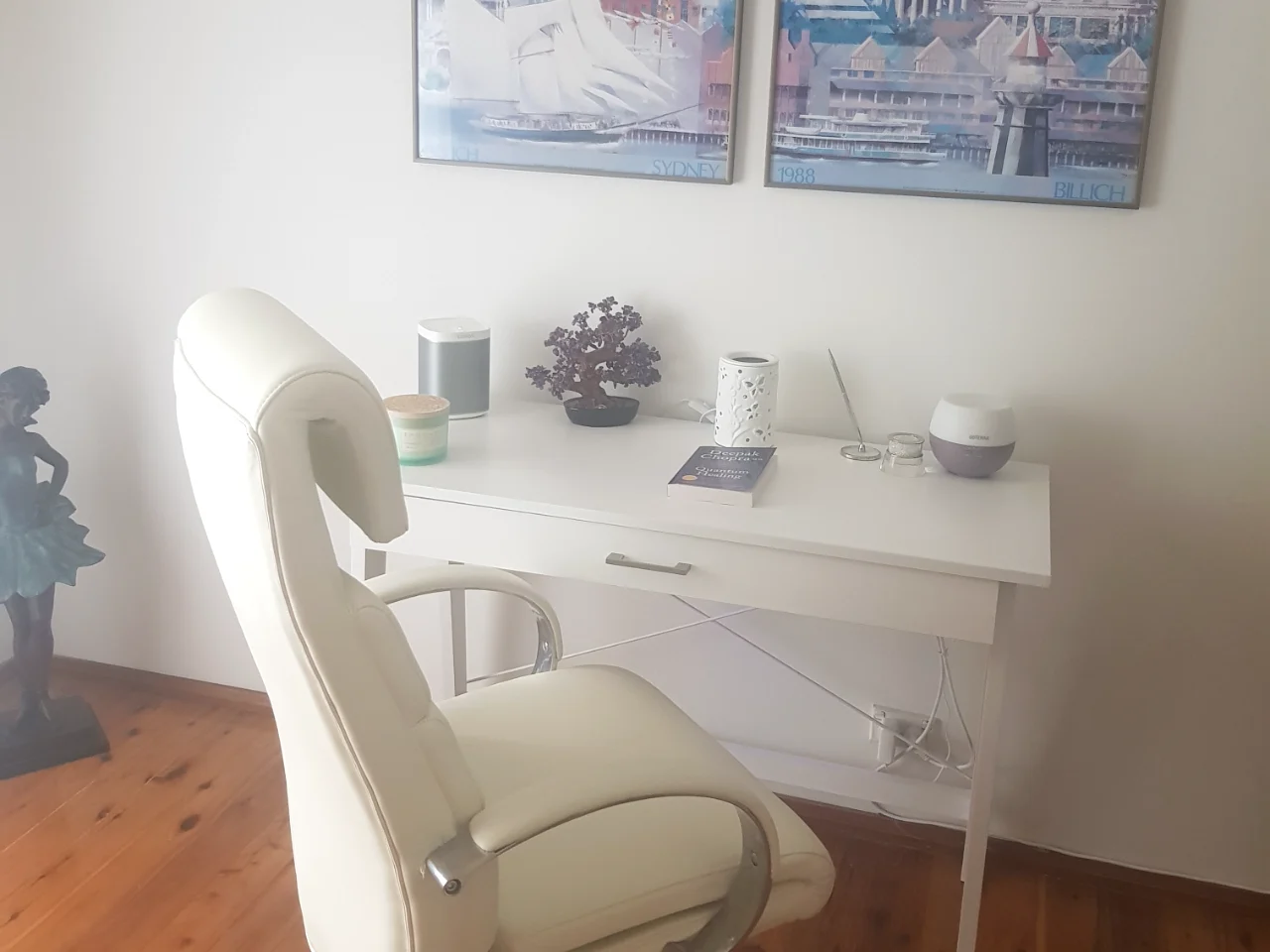 Angela's calm, light-filled consulting room in Minto, Macarthur — a white desk and chair with plants and a diffuser