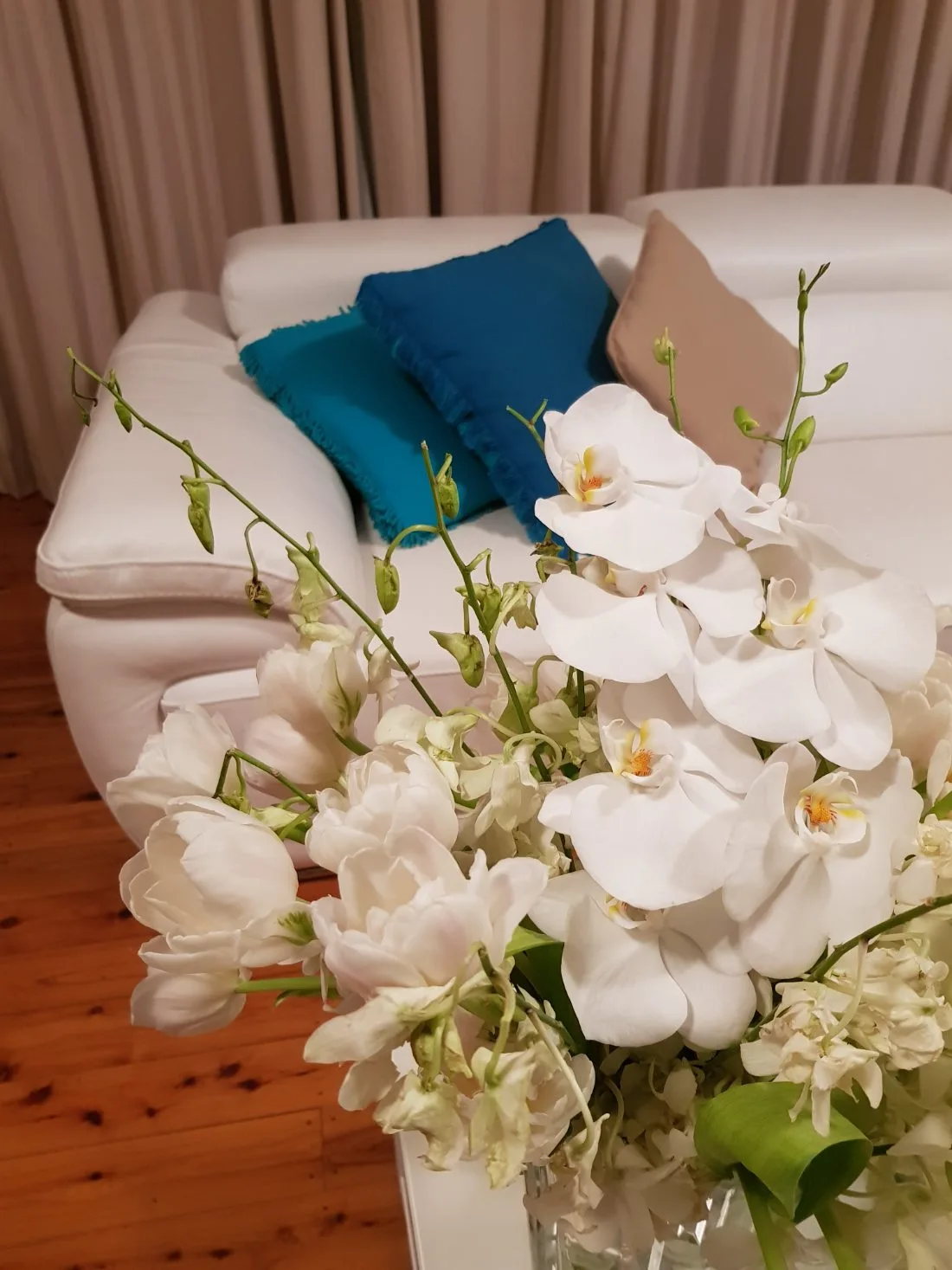 A comfortable white sofa with a teal cushion and fresh white orchids in a calm, light-filled home