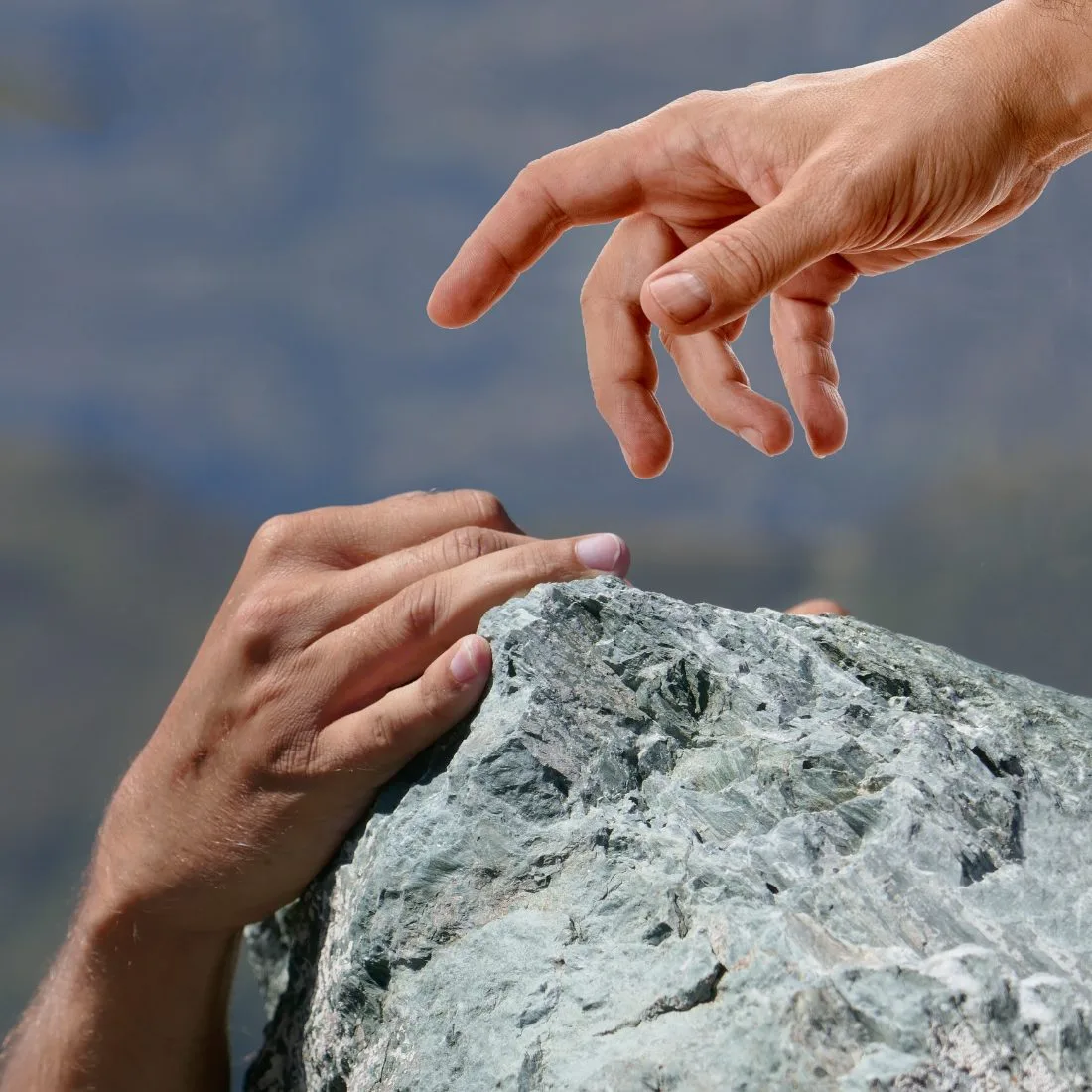 One hand reaching down to help another up a rock — support and reassurance through anxiety
