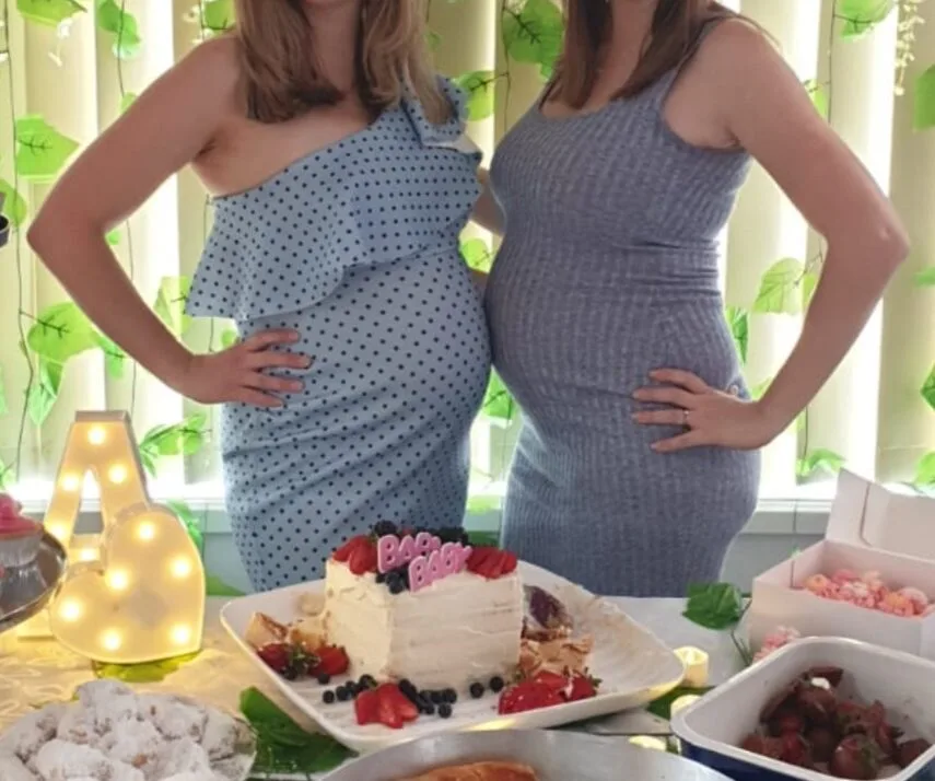 Two expectant mothers at a celebratory baby shower with cake and decorations