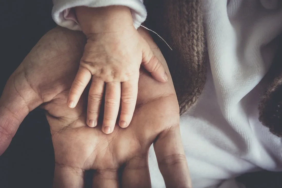 A baby's hand resting in an adult's open palm
