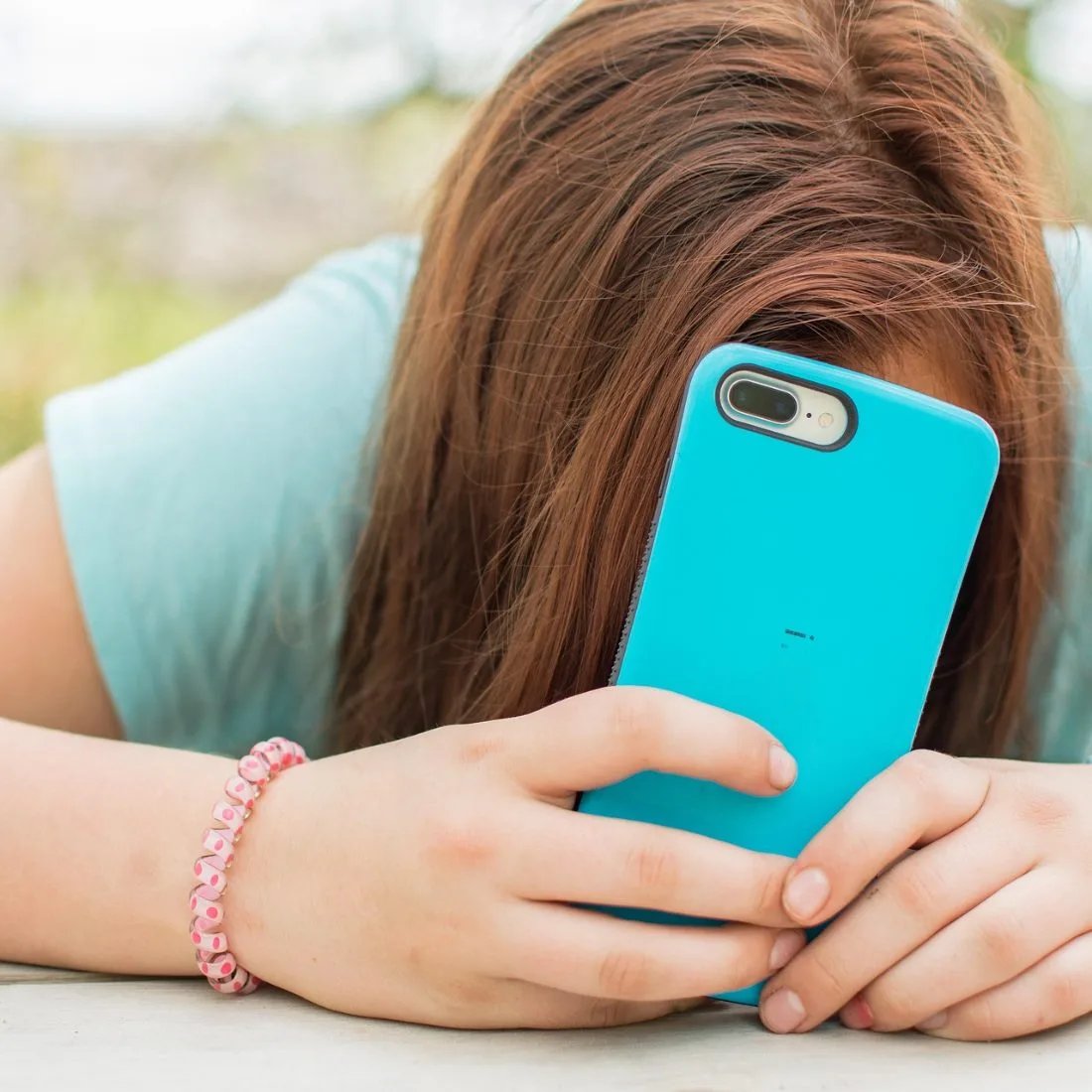 A teenage girl resting her head down, quietly absorbed in her phone