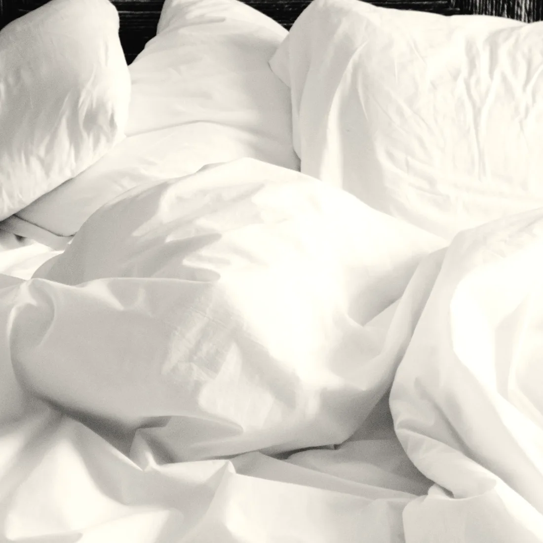 An unmade bed with soft white linen in quiet morning light
