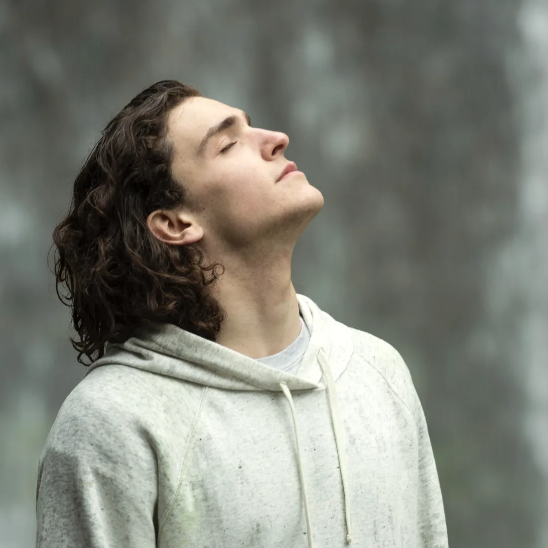 A young man standing outdoors with his head tipped back and eyes closed, jaw and neck relaxed