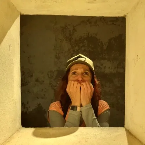 A person peering through a small opening with a nervous, fearful expression